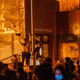 Flames from a nearby fire illuminate protesters standing on a barricade in front of the Third Police Precinct on May 28, 2020 in Minneapolis, Minnesota, during a protest over the death of George Floyd, an unarmed black man, who died after a police officer kneeled on his neck for several minutes.